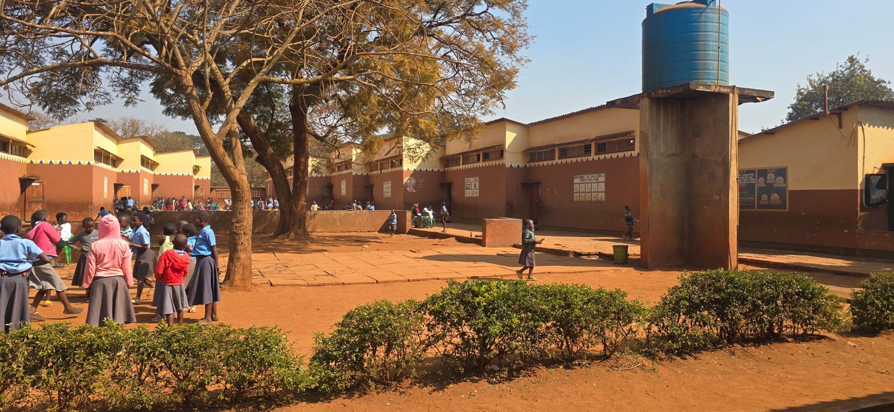 Learners in blue uniforms on the assembly ground beside the water tower and classroom blocks